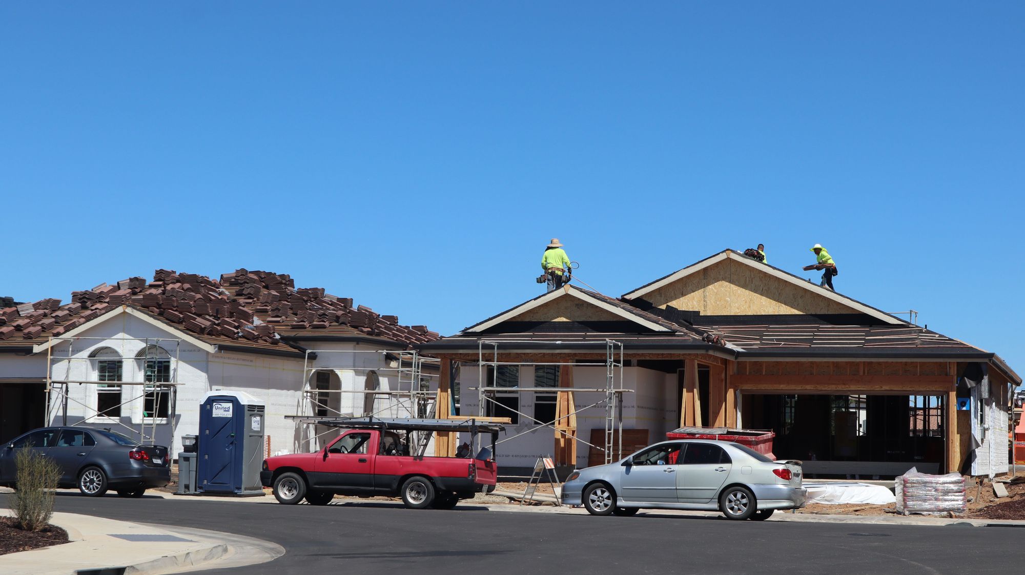 Roofing crew installing shingles on a new home under a clear blue sky